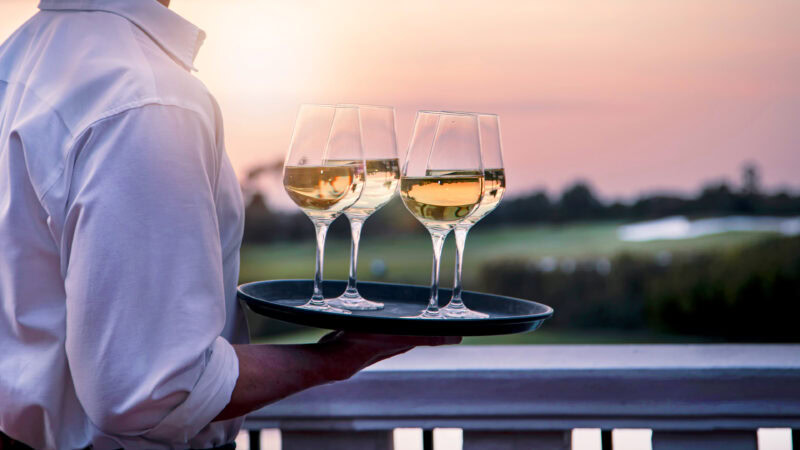 a person holding a tray with wine glasses - All inclusive Golfhotels