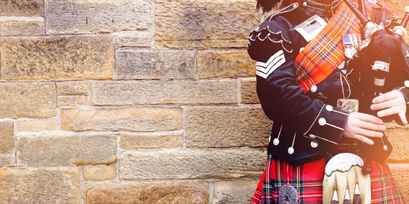 EDINBURGH, SCOTLAND, 24 March 2018 , Scottish bagpiper dressed in traditional red and black tartan dress stand before stone wall. Edinburgh, the most popular tourist city destination in Scotland.